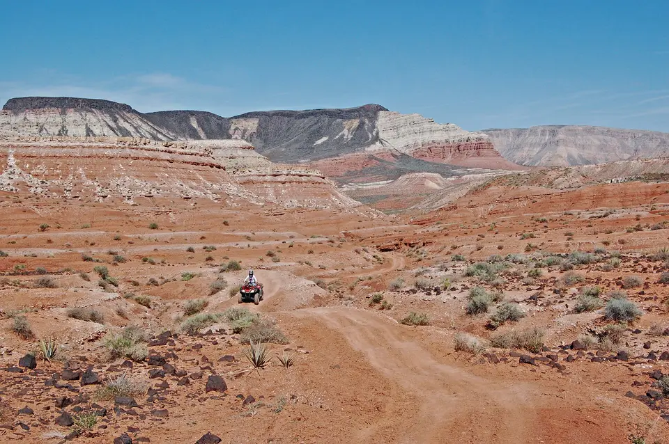 An ATV rider on a red-dirt two-track below layered cliffs in the Fort Pearce Wash OHV area
