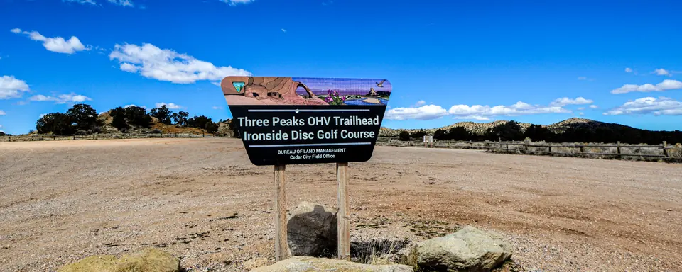 The Three Peaks OHV Trailhead sign and boulders at a gravel trailhead near Cedar City, Utah